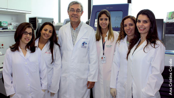 Fotografia da equipe: são cinco mulheres e um homem, todos estão de jaleco, no laboratório