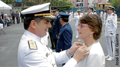 Fotografia com Helena Nader recebendo uma condecoração de um oficial da marinha