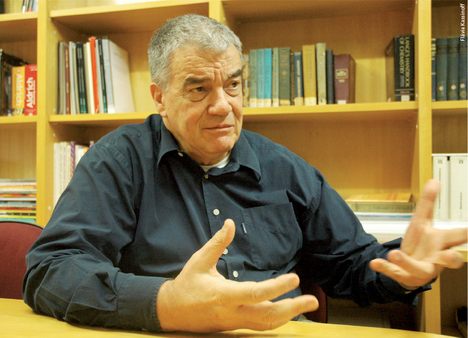 Foto do pesquisador Luiz Juliano, ele está sentado em um biblioteca concedendo a entrevista. Tem o rosto bastante expressivo e gesticula com as mãos