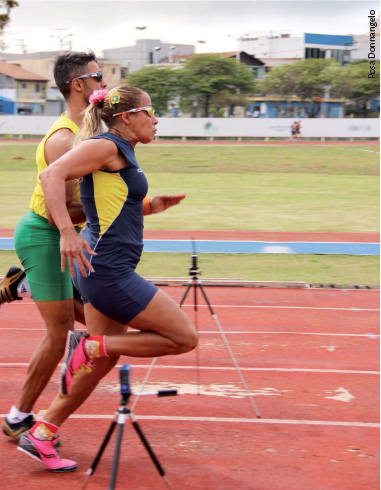 A atleta está correndo, ao lado de seu guia