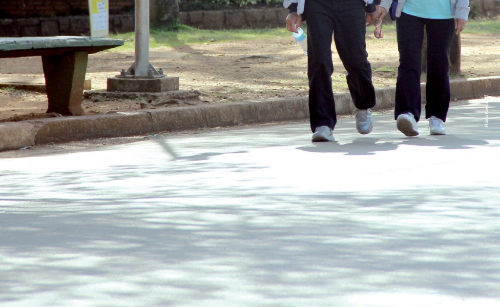 Fotografia que mostra duas pessoas caminhando em um parque - a imagem tem um corte e foca na pernas deles