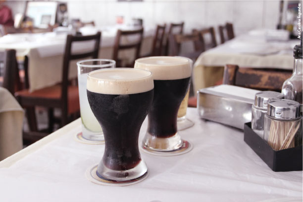 A fotografia mostra copos de chopp e outra bebida em uma mesa de bar