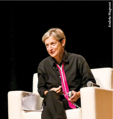 Fotografia de Judith butler, ela está em um palco, sentada em uma poltrona