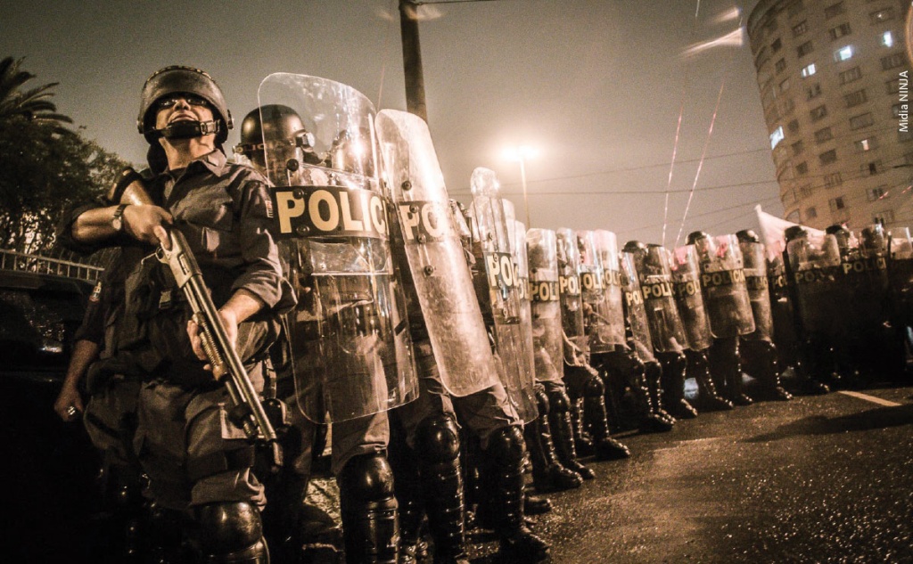 Fotografia mostra policiais, eles portam escudos e capacetes