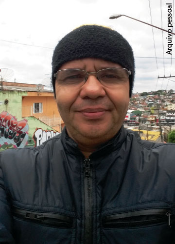 José Carlos Gomes da Silva, ele está de gorro e jaqueta preta, em um bairro de periferia