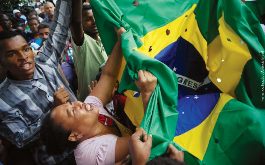 Enterro de jovens, uma mulher desesperada segura uma bandeira do Brasil cheia de furos