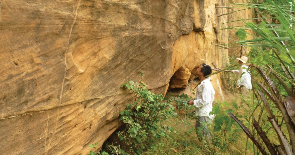 Dois pesquisadores examinam um paredão de pedra