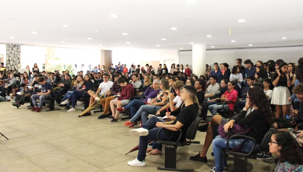 Imagem de um espaço amplo, com dezenas de pessoas sentadas