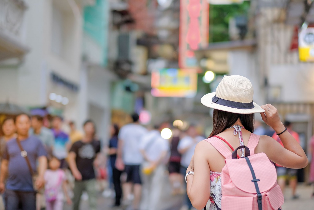 Imagem de uma rua de uma metrópole chinesa, com muitas pessoas ao fundo e uma mulher de chapéu em primeiro plano