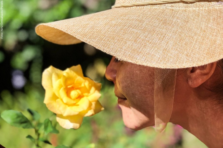 Mulher de chapéu cheirando uma rosa amarela