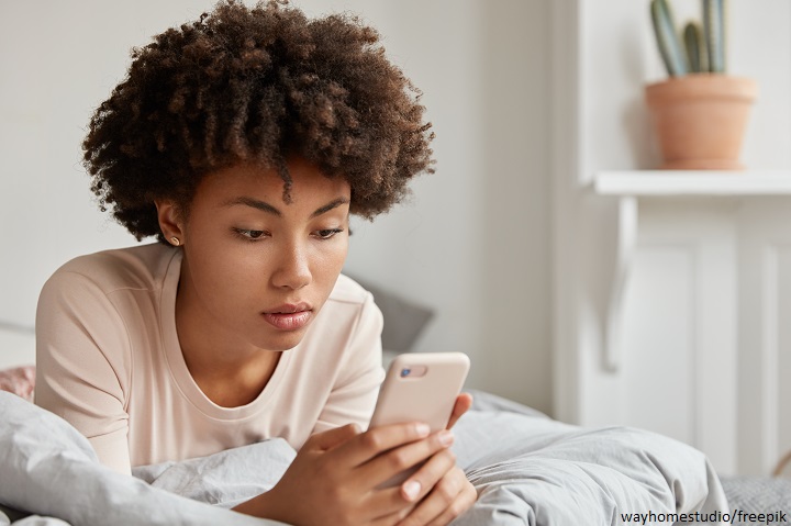 Jovem negra deitada de bruços olhando para o celular