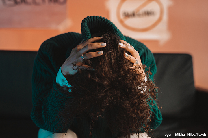 Jovem com a cabeça baixa e as mãos nela, es encolhendo