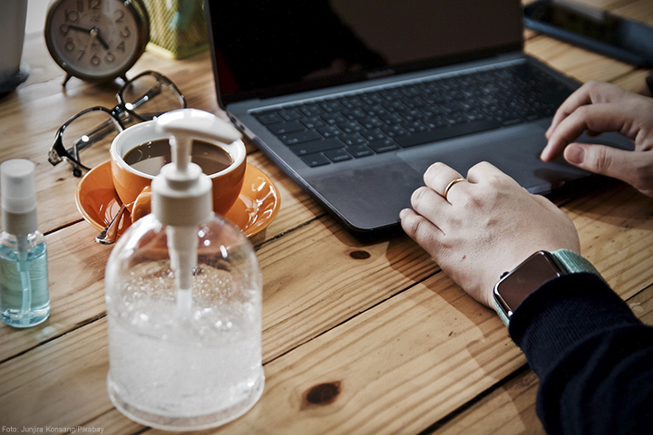 Pessoa utilizando um notebook em uma mesa com uma xícara de café e um pote de álcool em gel