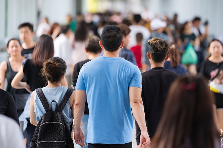 Multidão de pessoas caminhando; em primeiro plano algumas estão de costas