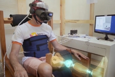 Imagem de um homem sentado utilizando equipamento de realidade virtual associada à estimulação vibro-tátil 