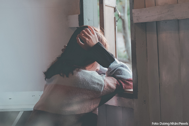 Mulher triste debruçada em uma janela