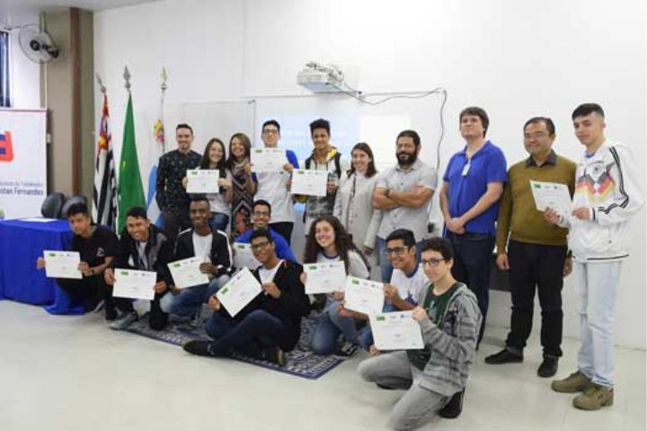 Jovens em pé em uma sala de aula segurando os certificados do curso