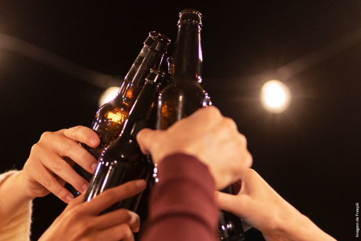 Mãos de jovens brindando com garrafas de cerveja; fundo escuro